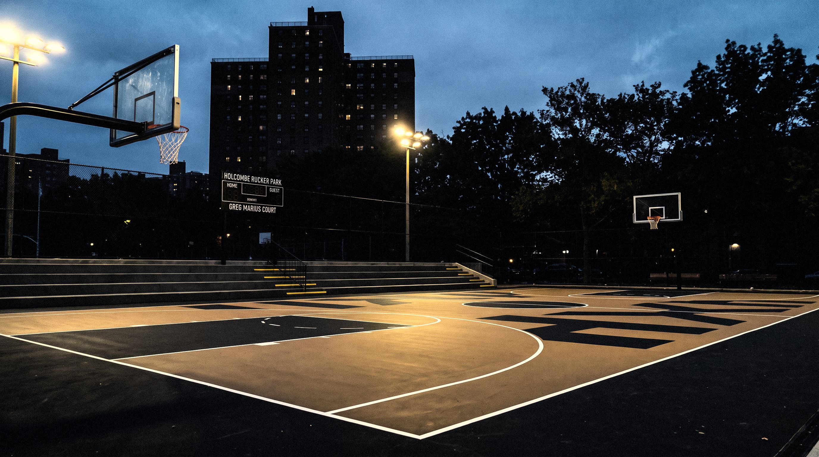 The renovated court at dusk, empty, the lights on, the Polo Grounds Towers behind (generated picture)
